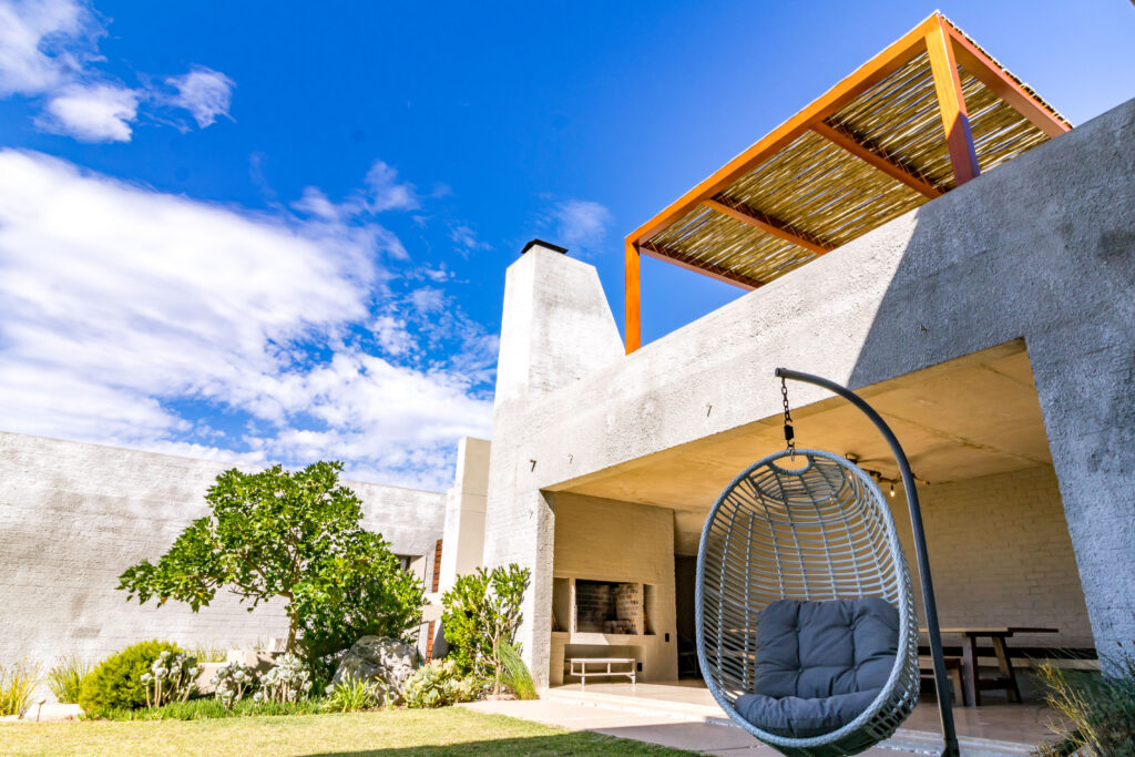 Concrete House courtyard with a suspended chair and angular timber roof against blue sky