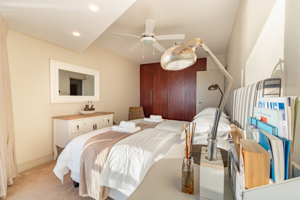 Sunlit twin bedroom with neutral linen and bedside reading lamp at Ocean View Apartment