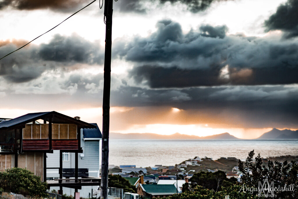 A timber coastal house beneath dramatic storm clouds